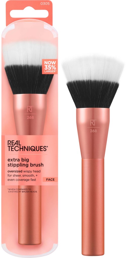 A makeup brush with pink handle and black and white bristles, in packaging that shows it's from Real Techniques.