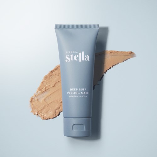 A blue tube of face mask with beige cream spread behind it on a light background.