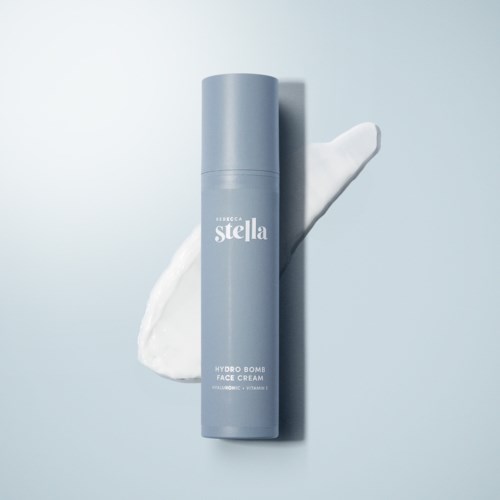 A blue bottle labeled 'Hydro Bomb Face Cream' standing upright on a smooth surface with a dollop of white cream nearby.