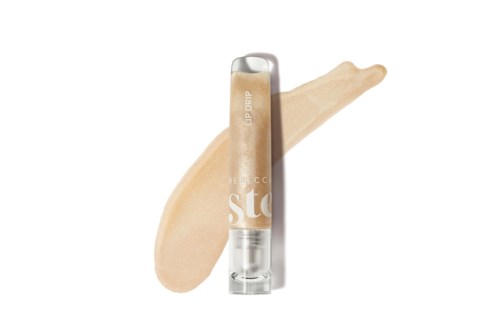 Lip gloss tube with a light beige color smeared behind it. Clear tube with silver cap and partially visible text.