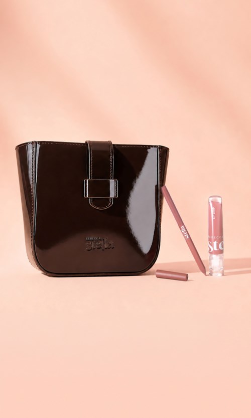 En blank svart veske med rem og spenne, sammen med rosa leppestift og lip gloss på rosa bakgrunn.