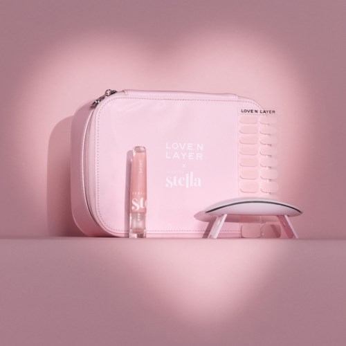 Pink bag, lipstick, and small white footstool on pink background. The bag has text and a zipper. The lipstick is standing upright.