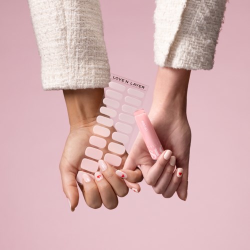 Person holding pink nail polish with a nail color palette, soft pink background, cozy sweater.