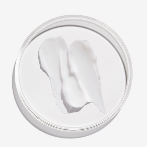 Een doorzichtige pot met witte crème en twee dollops erin, van boven gezien.