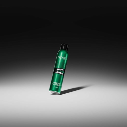 Eine grüne Haarwurzellifting-Spray-Flasche mit schwarzen Kappe steht auf einer schattigen grauen Oberfläche.