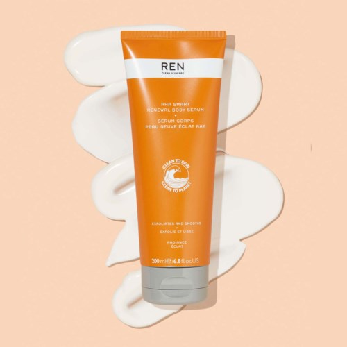 Orange tube av REN-kroppssserum med vit etikett, placerad på ljusbeige bakgrund med vita krämvågor.