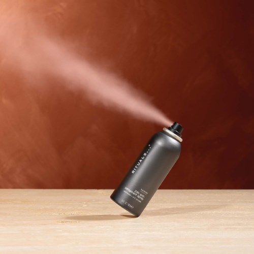 En svart bokspray som sender ut damp, med en trebordflate og en brun bakgrunn.
