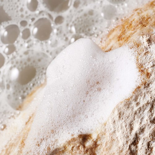 Eine Hand hält ein Stück Brot mit Schaum und Blasen, umgeben von Mehl.