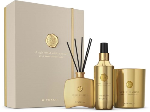 Goldfarbene Duftprodukte mit schwarzen Sticks, eine Sprühflasche, ein Glas und ein hellfarbenes Notizbuch mit goldener Beschriftung.