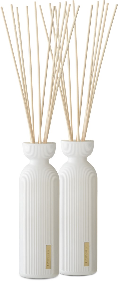 Två långa vita vaser med ribbor håller långa pinnar, vilket skapar en enkel och elegant inredning.