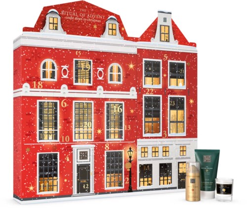 Ett rött adventskalendshus med fönster, ljus och numrerade dörrar, dekorerat för jul, med skönhetsprodukter framför.