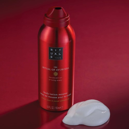Eine rote zylindrische Flasche mit Bodylotion und schwarzem Etikett, daneben weißer Schaum auf rotem Hintergrund.