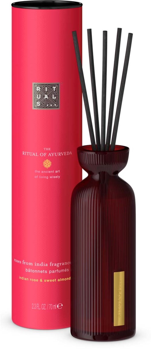 Ein roter und schwarzer Duftdiffusor mit Stäbchen, neben einer langen rosa Verpackung mit der Aufschrift 'The Ritual of Ayurveda'.