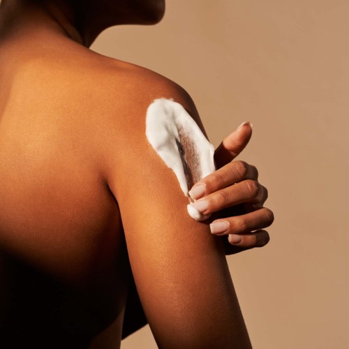 A person applies white cream on their shoulder, holding it with only their thumb and fingers.