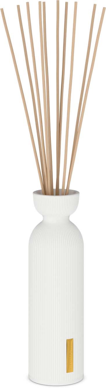 Eine weiße Vase mit Holzstäbchen, wahrscheinlich Duftstäbchen, und einem kleinen goldenen Etikett am Boden.