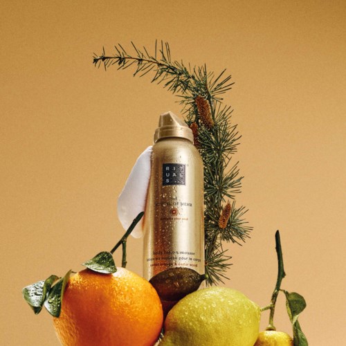 A can of skincare mousse stands next to a small pine branch with pine cones, orange, and green leaves.