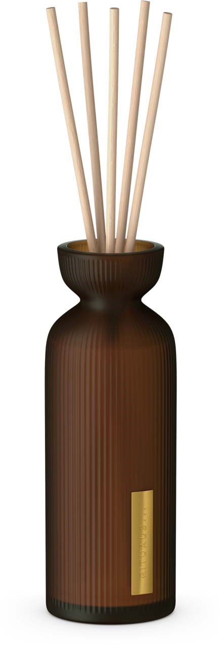A brown vase holds five light-colored reed sticks, used for diffusing scents or air freshener.