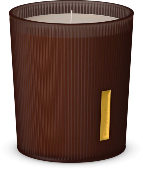 A brown candle with a gold label, in a ribbed container, with a white wick on top.