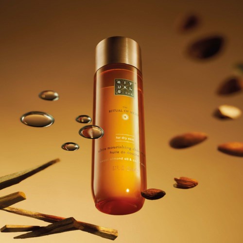 A skincare bottle surrounded by almonds, oil drops, and wooden sticks, with warm lighting emphasizing a luxurious feel.