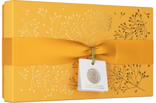 A yellow gift box wrapped with a yellow ribbon, decorated with white and dark brown leaf patterns, and a tag hanging.