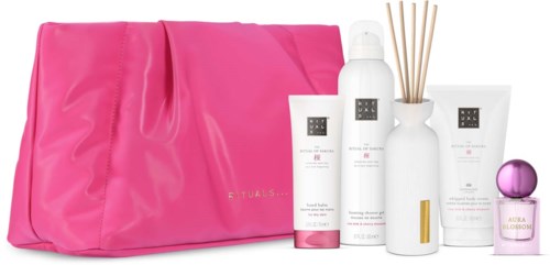 Set med hudvårds- och hemdoftprodukter framför en rosa väska, inklusive flaskor, diffuserpinnar och parfym.