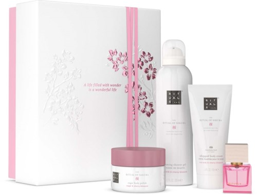 Ein Geschenkkarton mit weißer Verpackung, rosa Band und vier Pflege- oder Schönheitsprodukte in weißen und pinkfarbenen Behältern.