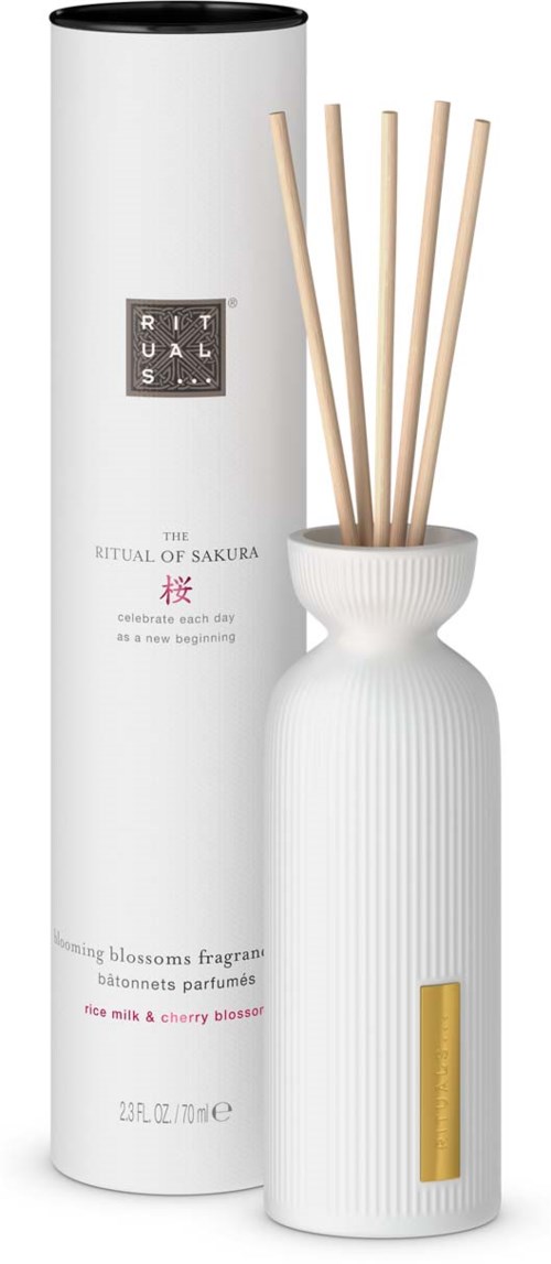 A white diffuser bottle with thin sticks inside, placed next to a cylindrical white packaging with text.