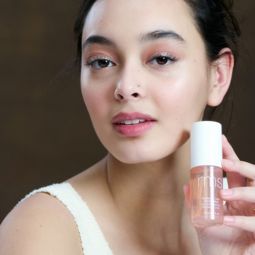 A young woman holds a small bottle of skincare product close to her face, with clear and smooth skin, smiling softly.