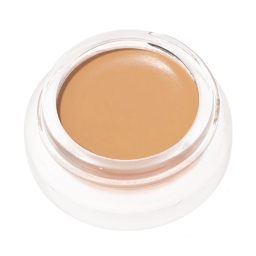 A small glass container filled with beige-colored cream or concealer.