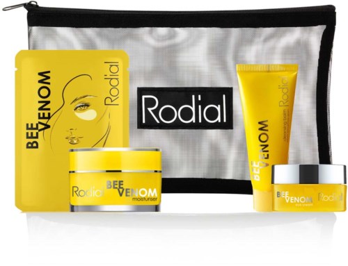 Skincare products, including creams and gel, in yellow and white packaging, with a travel bag in the background.