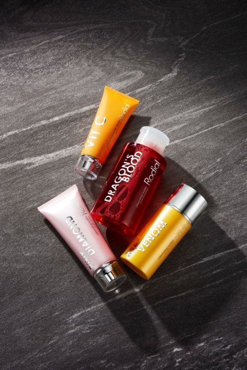 Four small cosmetic bottles and tubes with colorful labels on a dark surface.