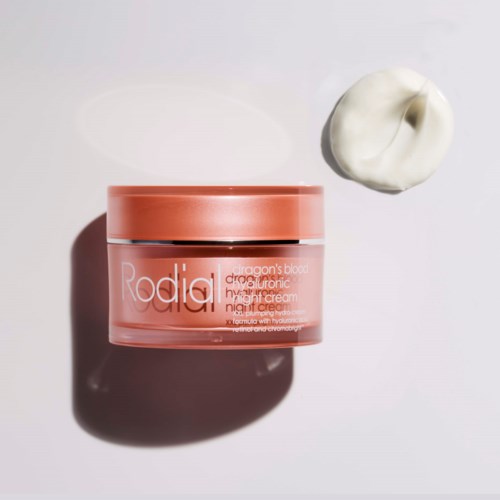 Een roze container met gezichtscrème en een dollop witte crème ernaast op een witte achtergrond.