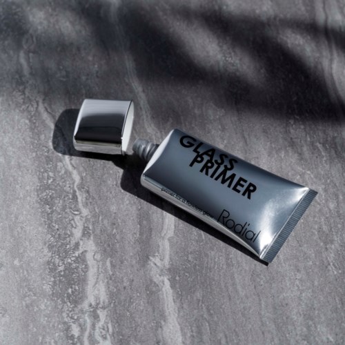 A tube of glass primer and its silver cap on a gray surface. The tube has black text and a shiny surface.
