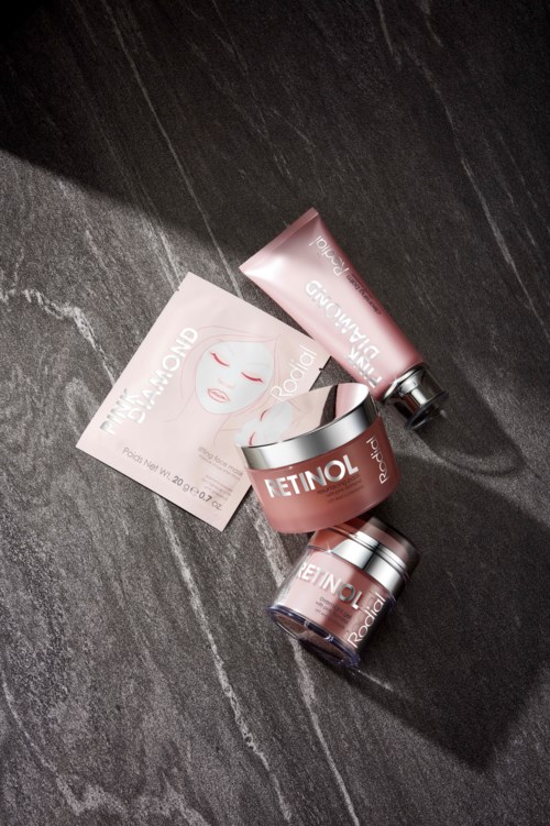 Skincare products, tubes, jars, and a face mask packet on a dark surface.