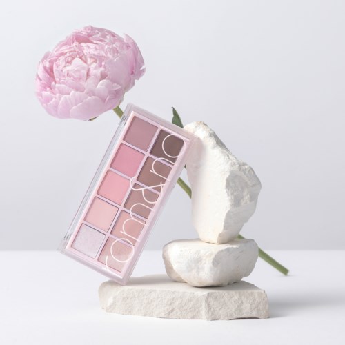 A pink flower, makeup palette, and white stones stacked in a balanced arrangement.
