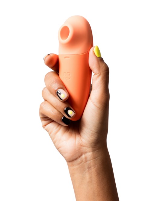 A hand holds a small, orange device with a rounded top and a hole, resembling a personal massager or gadget.
