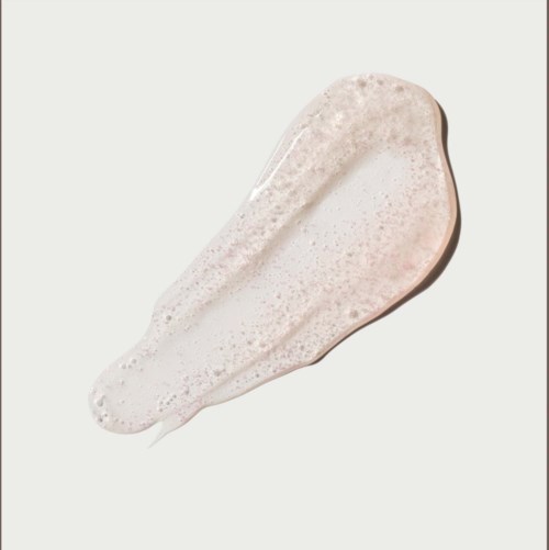 Een dot lichtroze crème of lotion met schuim erop, uitgespreid op een witte achtergrond.