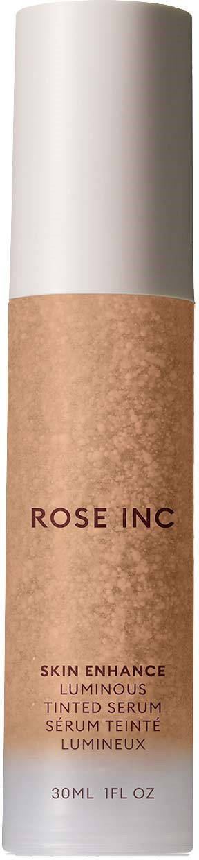 A tall, cylindrical skincare bottle with a white cap and beige body labeled 'ROSE INC' and 'Skin Enhance Luminous Tinted Serum.'