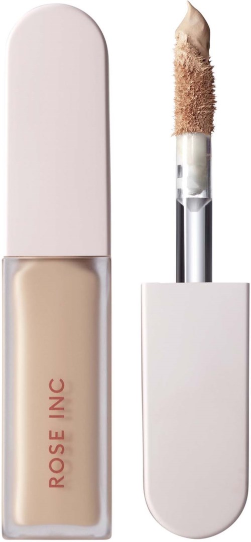 A makeup concealer with a white cap and beige liquid inside, labeled 'ROSE INC' on the bottle.