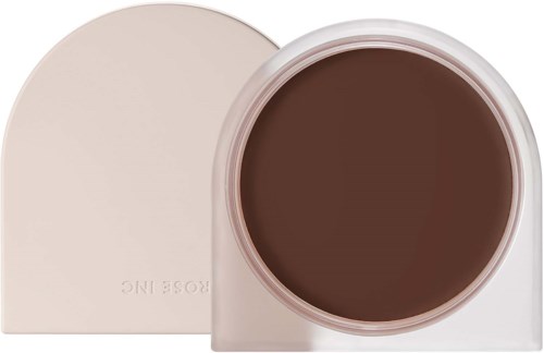 A round, dark brown makeup face powder container with a white lid. The brand name 'ROSE INC' is visible.