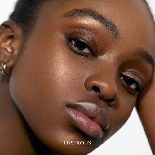 Close-up of a woman's face with glowing skin, dark eyes, and full lips. She looks calm and confident.