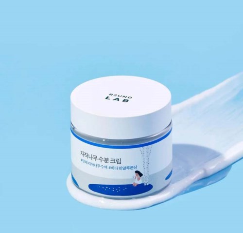A small white jar labeled 'ROUND LAB', with some cream spilled nearby on a blue surface.