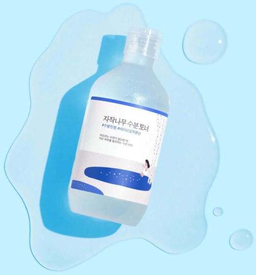 Eine Flasche liegt auf einer blauen Oberfläche mit Flüssigkeit drumherum. Die Flasche hat ein Etikett mit Text und Bild.