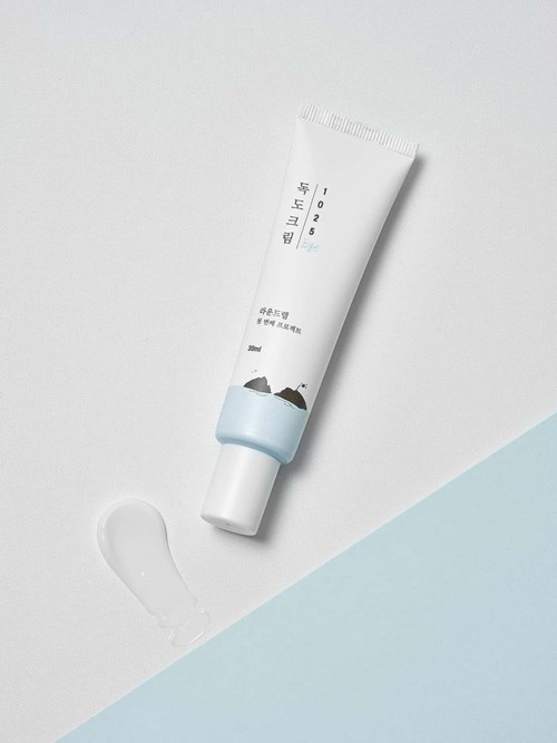 Eine Tube Creme mit koreanischem Text und kleiner Illustration, auf weißem und hellblauem Hintergrund.