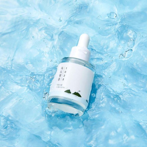 Eine Tropfenzapfeflasche schwimmt in klarem, blauem Wasser mit Blasen, mit minimalistischem Etikett und ruhigen Wellen.