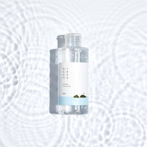 A clear bottle with blue label, surrounded by water ripples, casting a shadow on a white surface.
