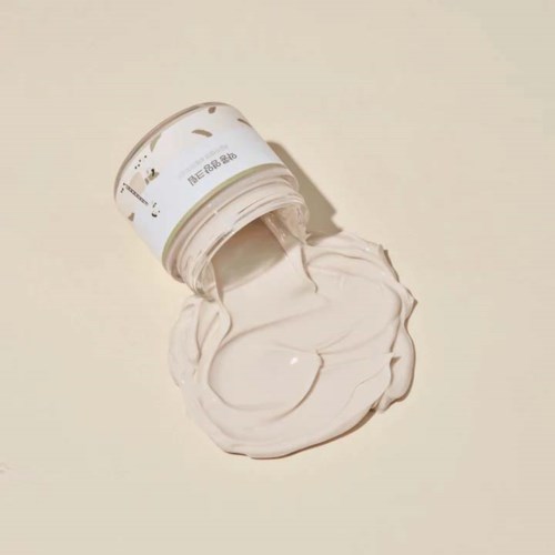 Eine weiße Creme oder Lotion wird aus einem kleinen Behälter auf eine einfache Oberfläche verschüttet.