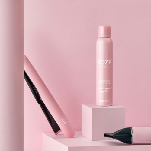 A pink can, a pink hairbrush, and a black hairdryer on pink and white background. The scene looks styled and neat.
