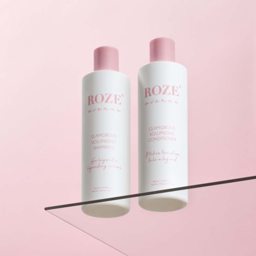 Zwei weiße Flaschen mit pinken Deckeln und pinkem Text auf rosa Hintergrund, eine ist Shampoo, die andere Spülung.