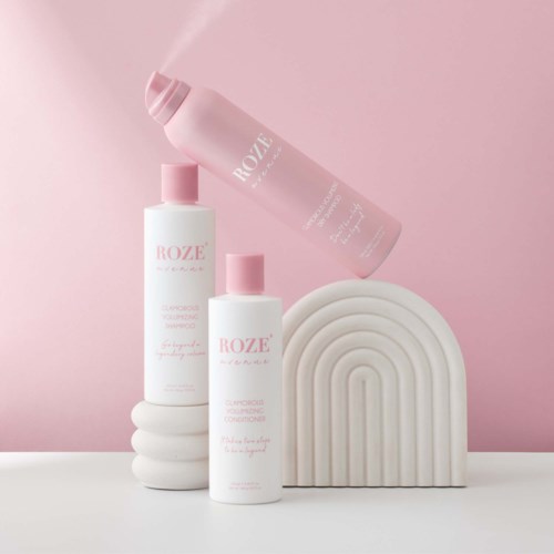 Drei Flaschen Shampoo und Conditioner mit rosa Verschlüssen, auf weißen gewellten Plattformen vor hellrosa Hintergrund.